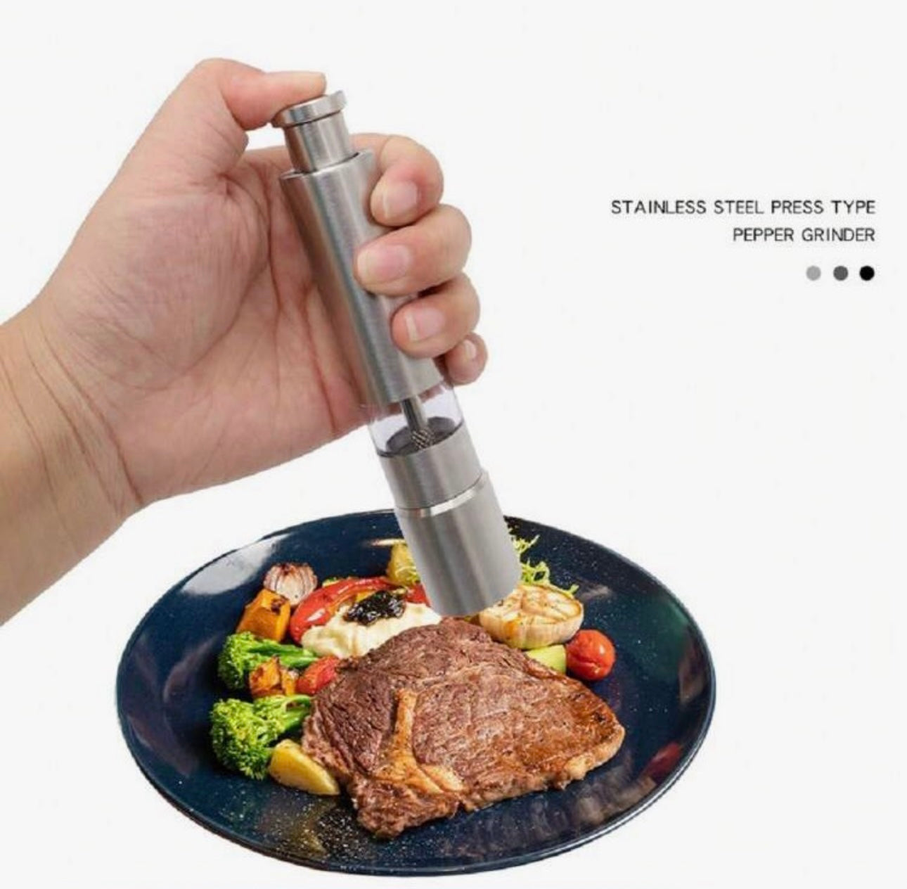 Hand holding a stainless steel pepper grinder over a plate of food on a white background