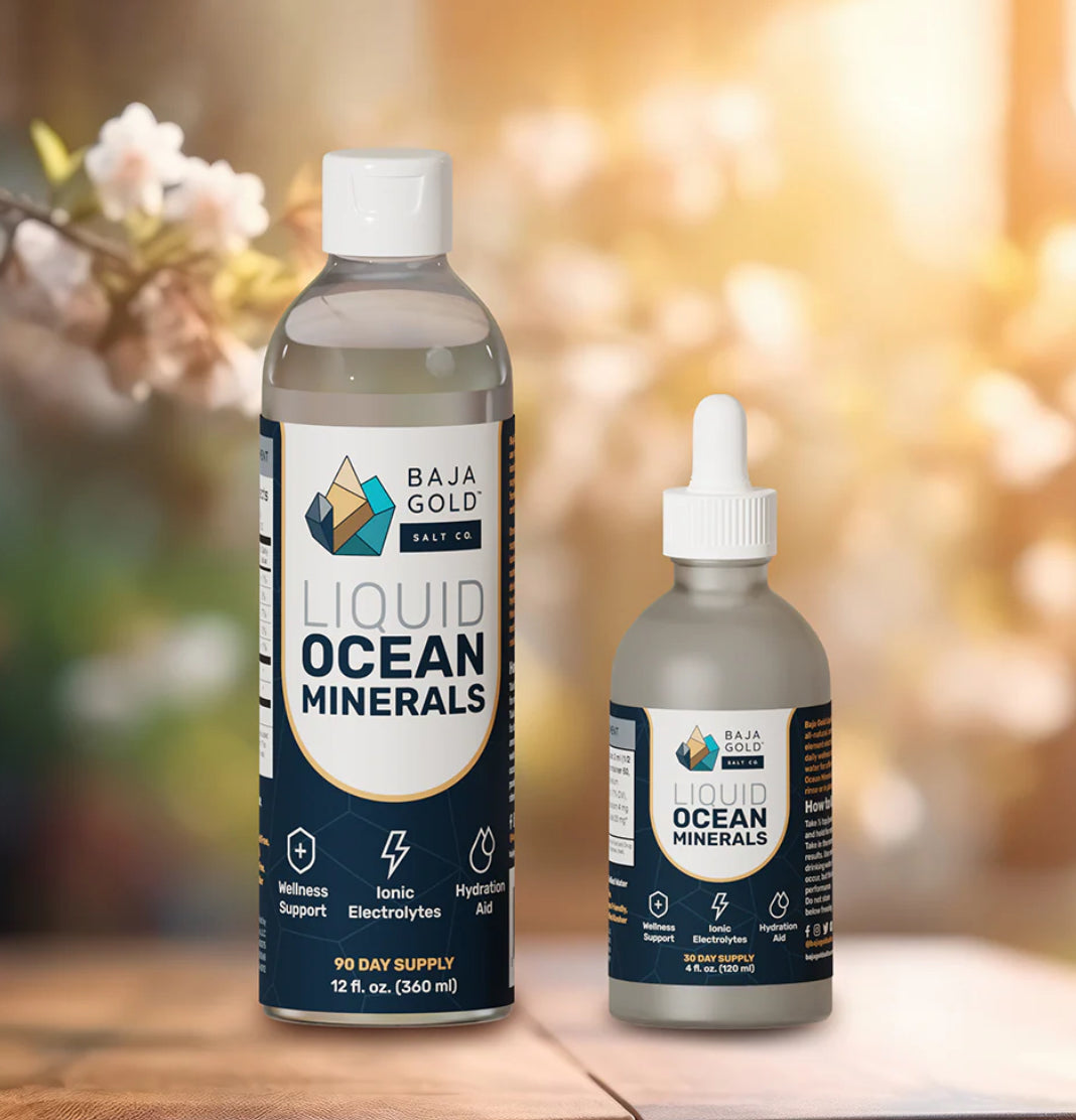 Two bottles of Baja Gold Liquid Ocean Minerals on a wooden surface with a blurred natural background.