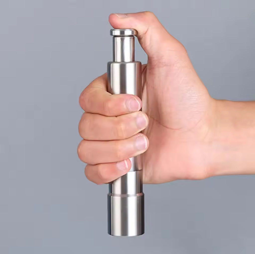 Hand holding a metallic pepper grinder against a gray background