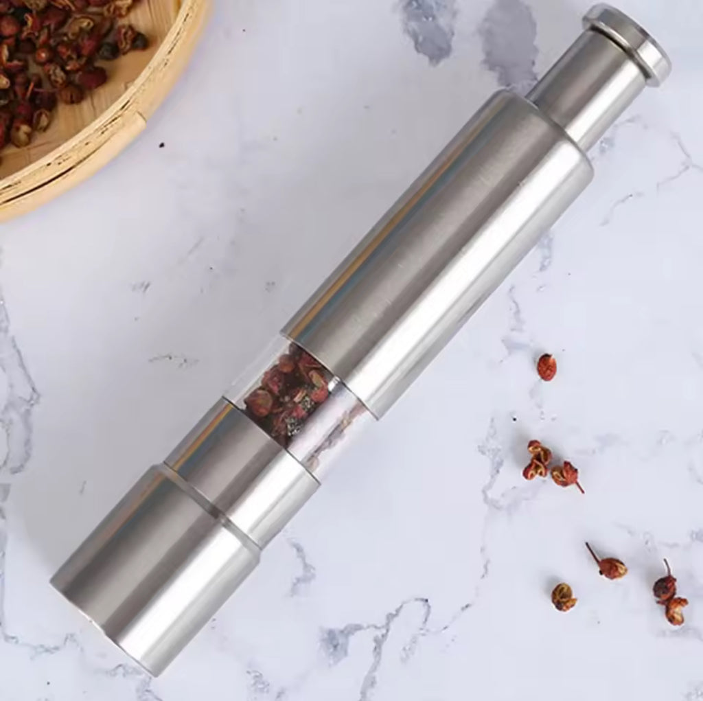 Stainless steel pepper mill with red peppercorns on a marble surface